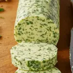 Beurre à l'ail et au persil fait maison tranché planche bois herbes fraîches